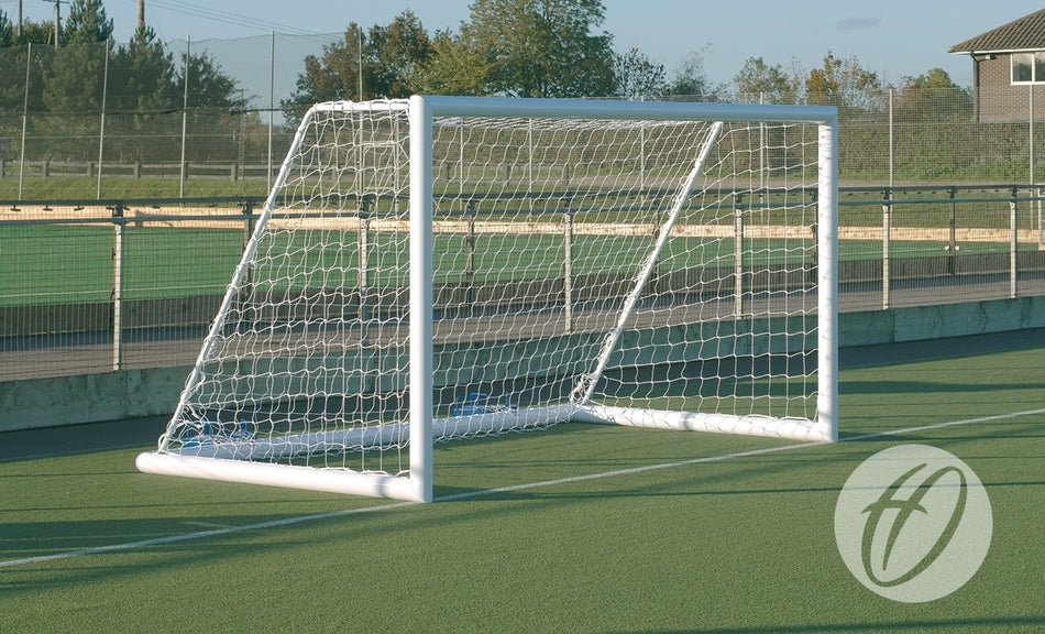 A Harrod Sport 3G Portagoal - 7V7/5V5 with Hi-Raise wheels stands on a green artificial turf field, near a fence and trees beneath a clear sky.