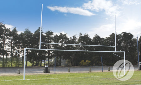The Harrod Sport Senior Combination Football/Rugby Posts are installed on a grassy field, with trees, a fence, and a road in the background under a partly cloudy sky.