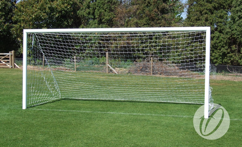 A Harrod Sport 4G Stadium Goal - 9V9 with a net is positioned on a green grass field, with trees and a fence in the background on a sunny day.