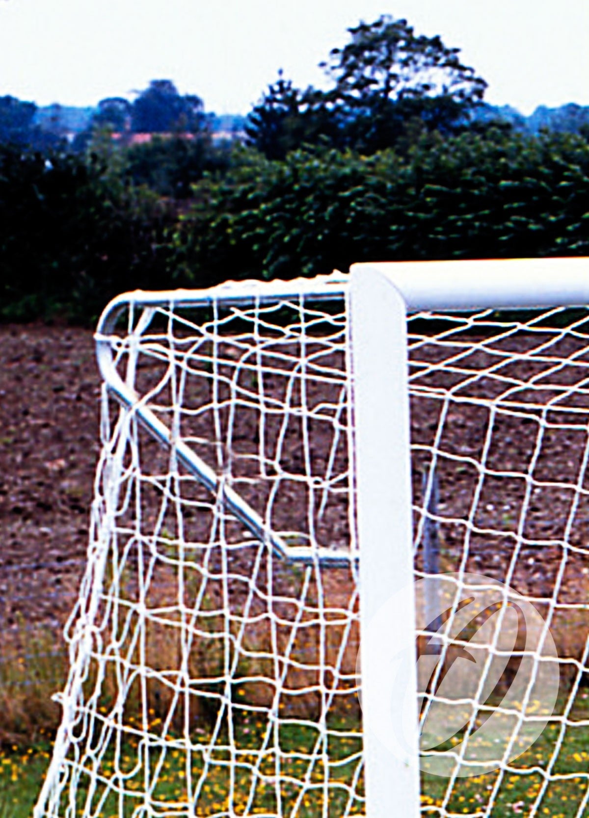 A close-up of the Harrod Sport Elbow Net Support for 3G Stadium Club Goal, highlighting sturdy aluminium brackets on a white goal post and net, set on a grassy soccer field with trees and a cloudy sky in the background.