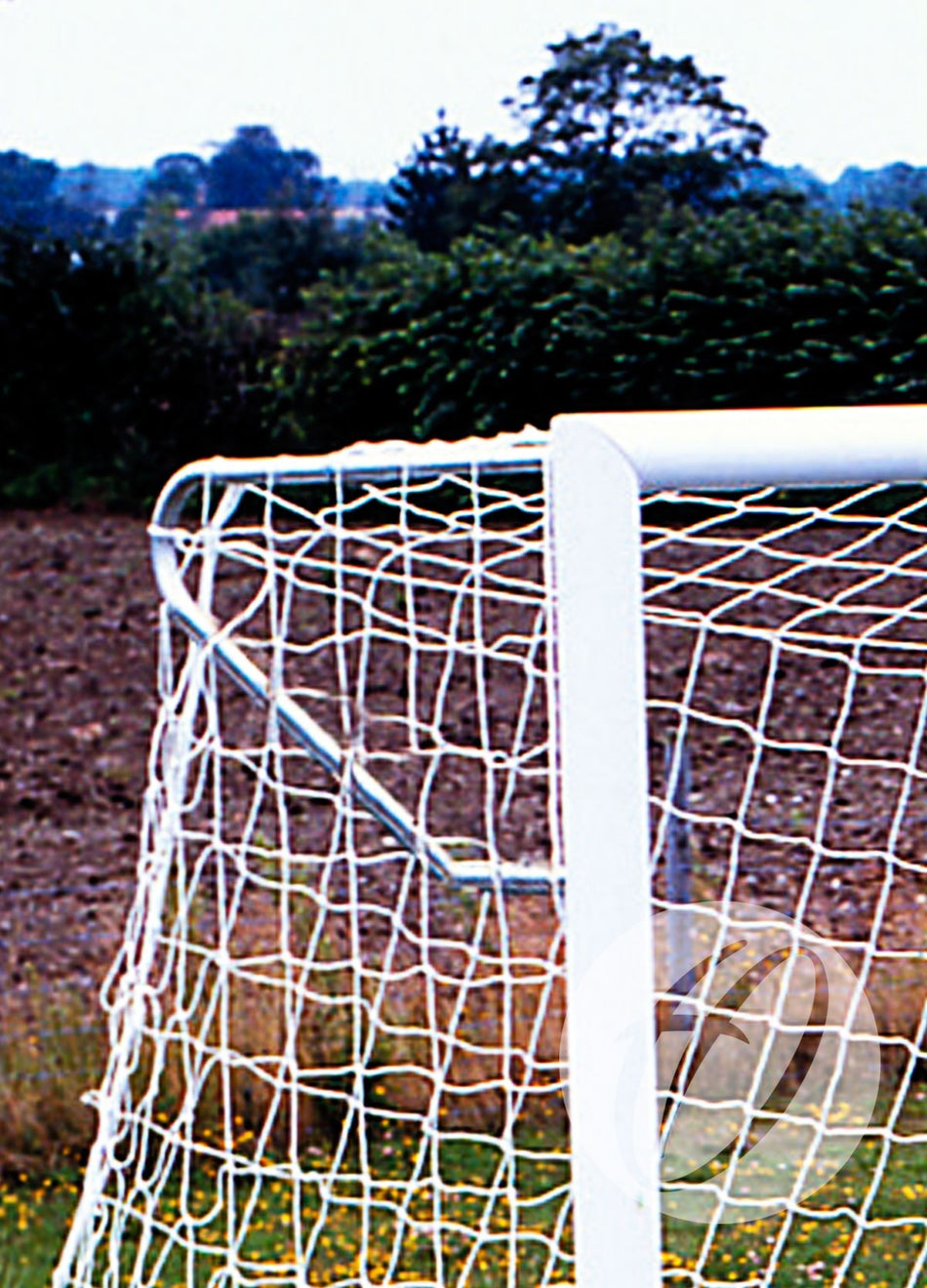 A close-up of the Harrod Sport Elbow Net Support for 3G Stadium Club Goal, highlighting sturdy aluminium brackets on a white goal post and net, set on a grassy soccer field with trees and a cloudy sky in the background.
