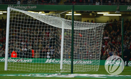 A soccer goal with a tangled net leans on the field, supported by the Harrod Sport Freehanging Net Support System – 4 Poles. A crowd fills the background, and a green barrier displays Worthington’s branding.
