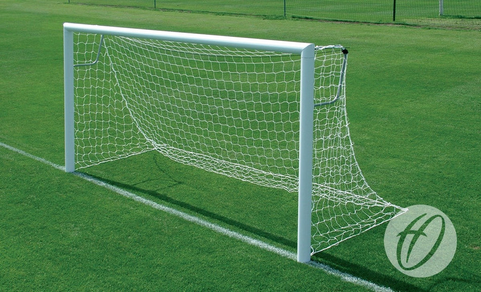 A Harrod Sport 4G Stadium Goal – 7V7/5V5, with a reinforced white aluminium frame and net, stands on a pristine grass field beneath a clear sky. A circular logo is visible in the corner of the image.