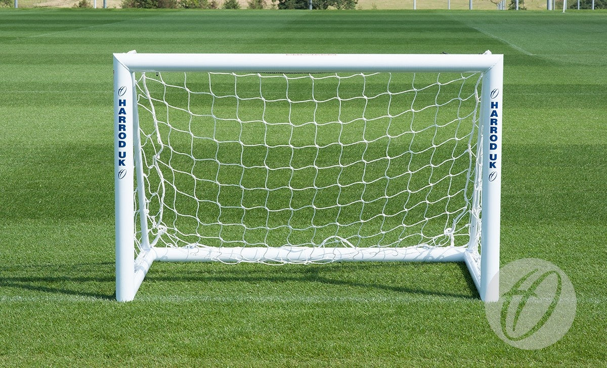 A 1.5M x 1.0M Mini Target Goal with Net by Harrod Sport stands on a well-manicured green field. The brand name "Harrod Sport" is printed vertically in blue on both aluminium goalposts, making it an ideal portable training aid for practice sessions or as a mini training goal.