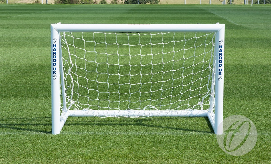 A 1.5M x 1.0M Mini Target Goal with Net by Harrod Sport stands on a well-manicured green field. The brand name "Harrod Sport" is printed vertically in blue on both aluminium goalposts, making it an ideal portable training aid for practice sessions or as a mini training goal.