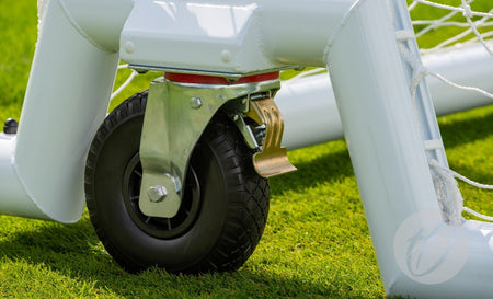 Close-up of a black wheel with metal bracket fixed to the base of a Harrod 4G Swivel Senior Portagoal by Harrod Sport on green grass, net visible in the background—perfect for Premier League coaches training on 4G pitches.