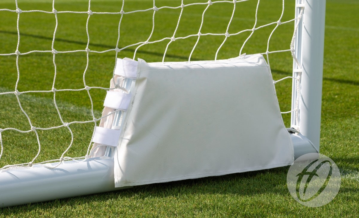 A close-up of a white rectangular safety pad attached to the bottom corner of a Harrod Sport 4G Swivel Weighted 7V7 / 5V5 Portagoal, positioned on green grass.