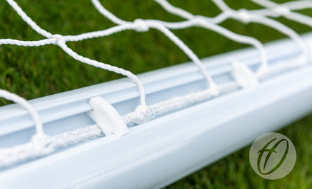 Close-up of a Harrod Sport 4G Swivel Weighted 16x6 Portagoal with white net attached by plastic clips on green artificial turf. A circular logo is shown in the bottom right—perfect for training sessions.
