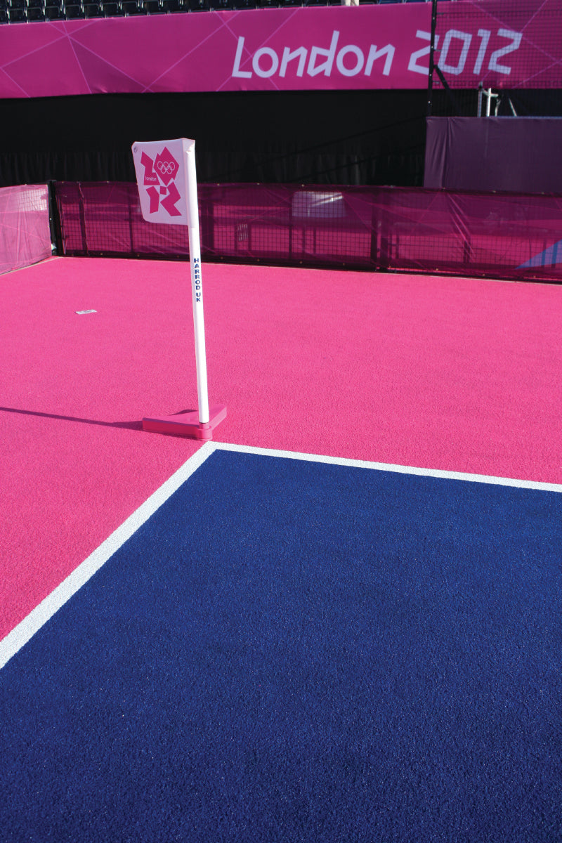 The Harrod Sport 1.5M High Corner Pole (50MM) & Base, seen at the London 2012 Olympics with a white pole offsetting the vivid pink and blue field hockey pitch, is an essential piece of hockey training equipment.