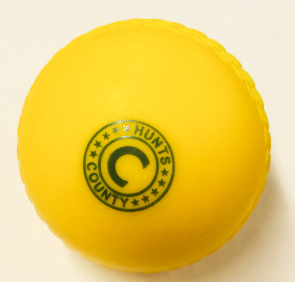 The Hunts County Flik Plastic Cricket Ball features a bright yellow design with a green circular pattern and the Hunts County logo, shown against a white background—ideal for Hunts County cricket fans.