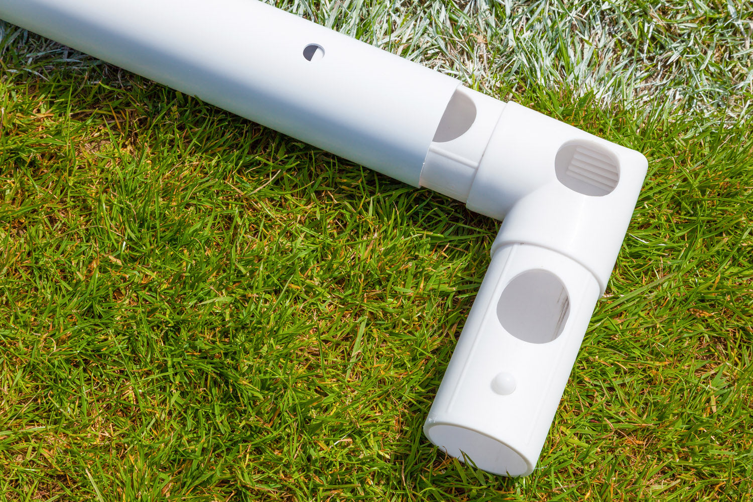 Close-up of a white uPVC joint forming a right angle between two pipes on grass near a white line—part of the Samba Sports Samba Match Goal 8 x 6 on a sports field.