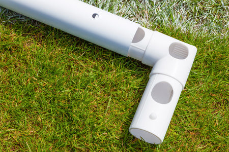 Close-up of a white uPVC joint forming a right angle between two pipes on grass near a white line—part of the Samba Sports Samba Match Goal 8 x 6 on a sports field.
