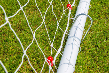 Close-up of the Samba Sports Samba Match Goal 8 x 6, showing its durable white uPVC frame on green grass, red clips securing the netting, and a metal stake fixing the goal firmly to the ground.