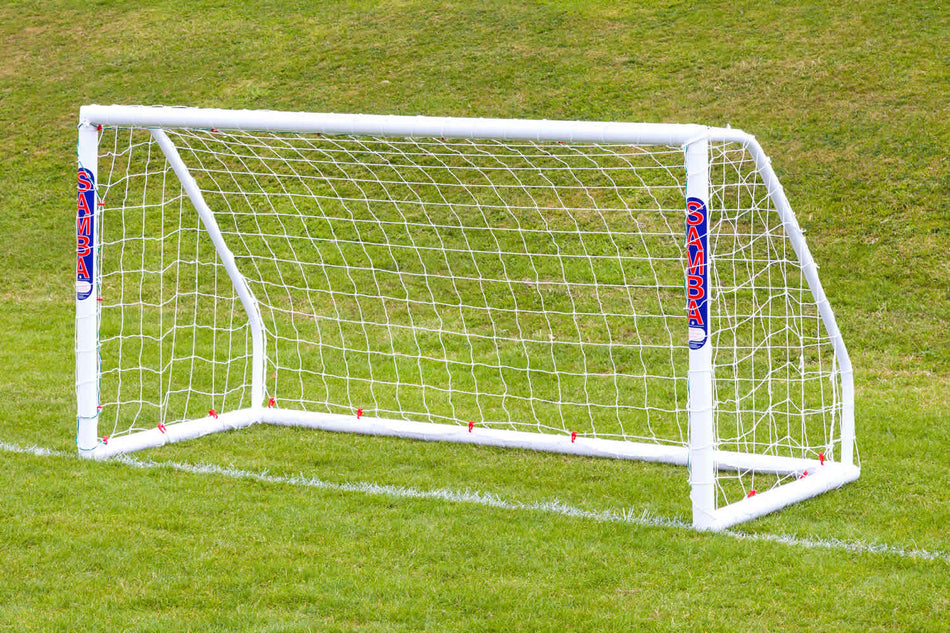 The Samba Sports Samba Match Goal 8 x 4, an easy-to-assemble white football goal with "SAMBA" printed vertically on its posts, stands with its net on a grassy field against a gently sloped background.