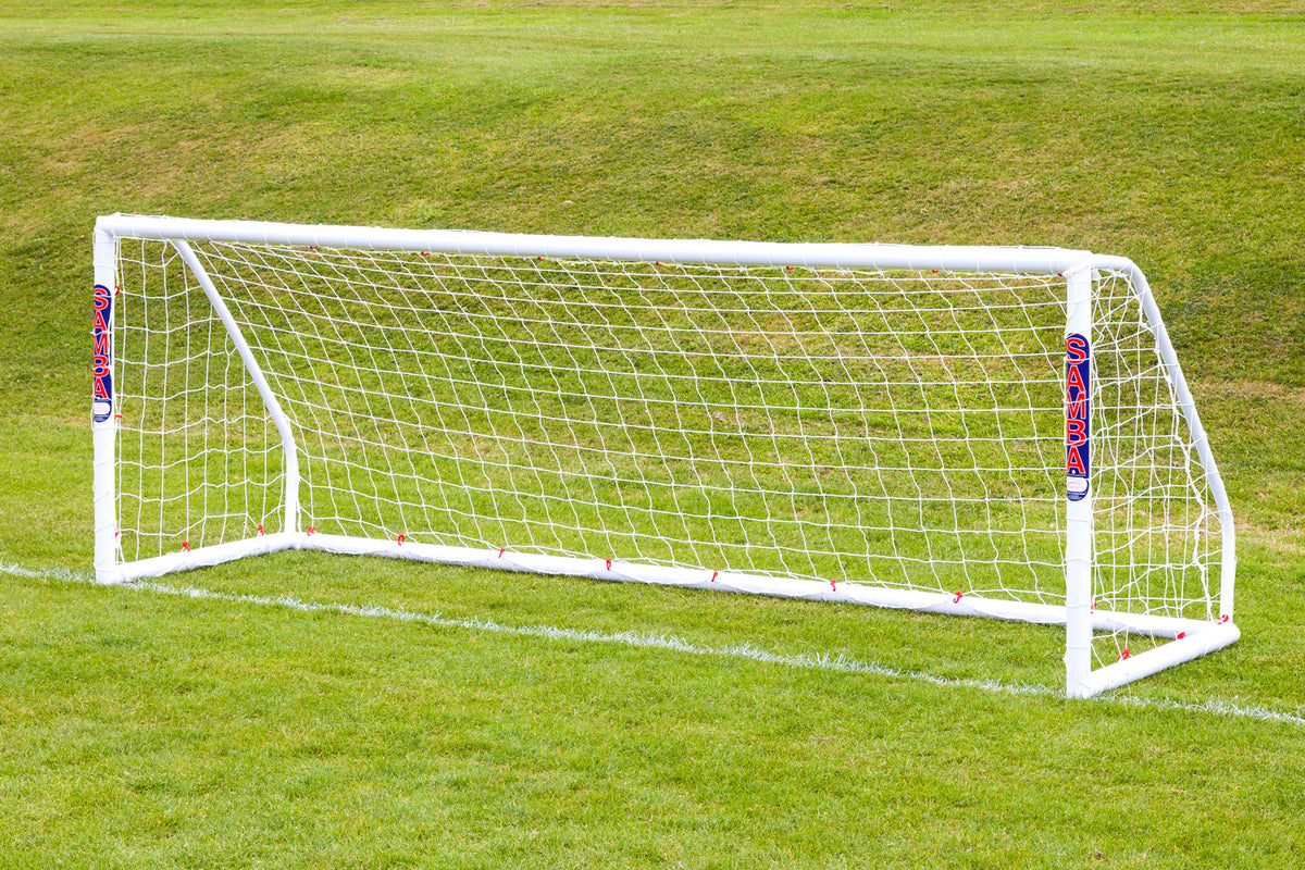 The Samba Match Goal 12 x 4 by Samba Sports, a white uPVC weatherproof football goal with net and SAMBA branding on side padding, stands on a grassy field with a sloped hill in the background.