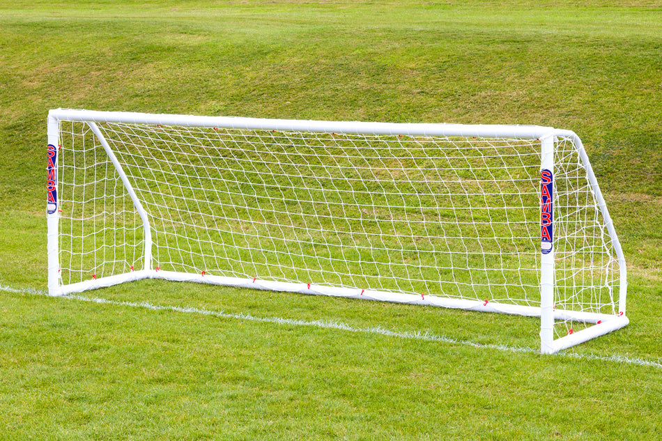 The Samba Match Goal 12 x 4 by Samba Sports, a white uPVC weatherproof football goal with net and SAMBA branding on side padding, stands on a grassy field with a sloped hill in the background.