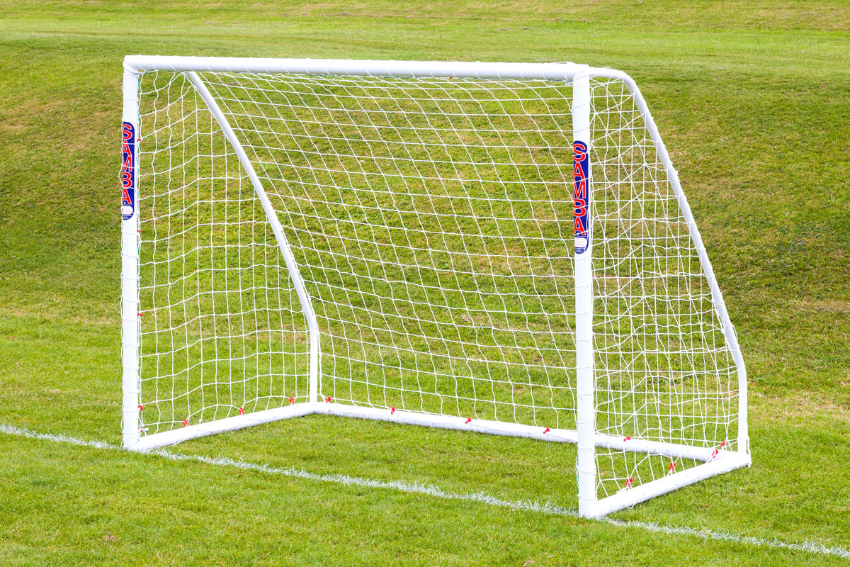 A Samba Sports Match Goal 8 x 6, made from high-impact uPVC with SAMBA branding, stands on a gently sloping grassy field with neatly mown green grass and includes a net.