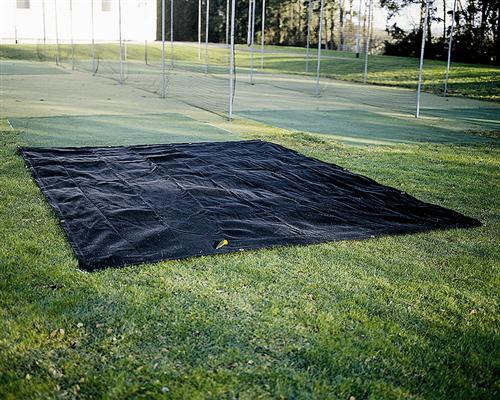 A Martin Berrill Sports Seed Germination Sheet, 4m x 25m in black, is laid flat on grass with sports nets and green turf nearby and trees surrounding the outdoor area.