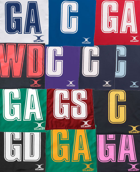 A grid of Gilbert Pro Patch Bibs in assorted colors, each displaying large white position initials for easy player ID. These netball training bibs feature the Gilbert logo at the bottom.