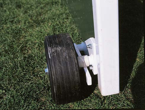 Close-up of a puncture-resistant rubber wheel from the Harrod Sport Flip Over Wheel Kit, mounted on the base of a white metal frame and resting on green grass, designed for use with outdoor steel hockey goals.
