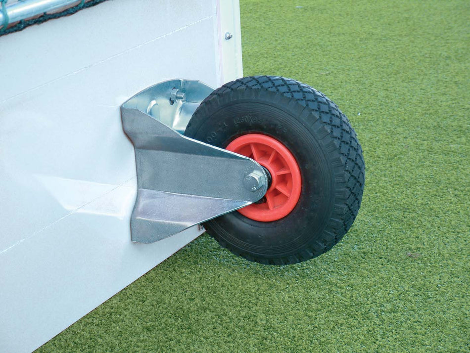 A close-up of the Harrod Sport Cellular Rubber Wheel Kit with a black puncture-proof wheel and red hub on a metal bracket, fitted to aluminium hockey goals, shown resting on green artificial turf.