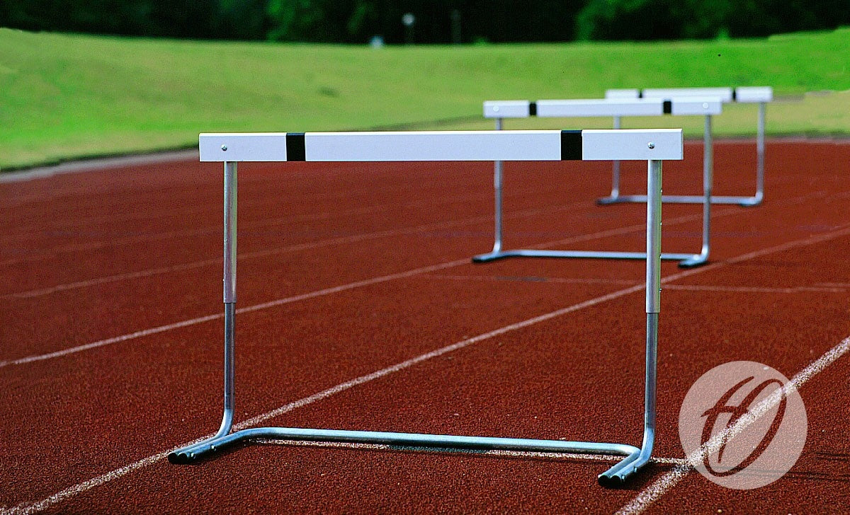Three Harrod Sport H8 Junior Practice Hurdles are set up evenly in a row on a red running track with green grass and trees behind, visible track lines, ideal for school and club use.