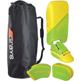 A black Grays sports bag sits next to a Grays G100 Junior Goalie Set in lime/yellow, which includes leg guards, kickers, hand protectors, and a left-hand blocker—all with protective dual-density foam.
