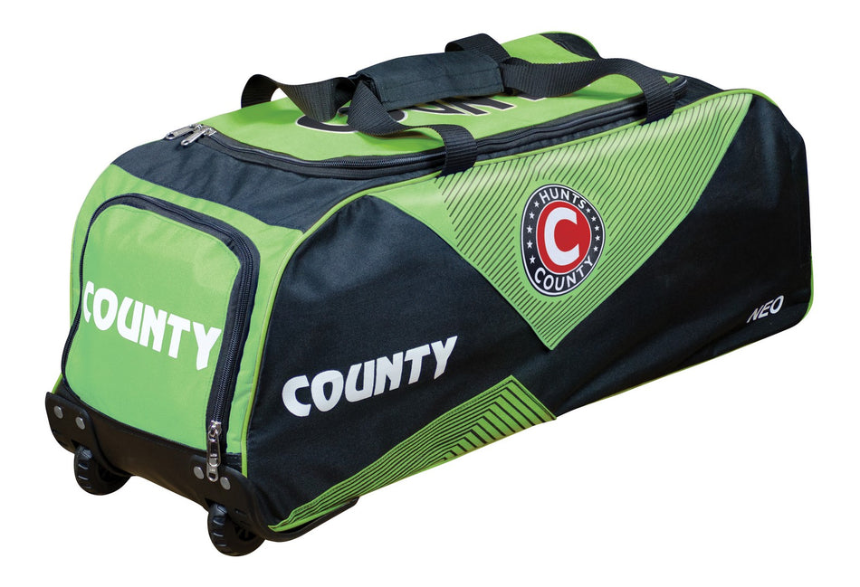 The Hunts County Neo Wheelie Cricket Bag in black/green has COUNTY on the side, a circular Hunts County logo, sturdy top handles, wheels, and multiple zip compartments for organized cricket gear storage.