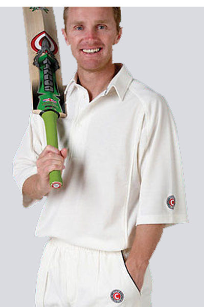 A smiling man wears a Hunts County Plain Cricket Shirt (3/4 Sleeve) and holds a cricket bat over his shoulder with one hand while the other is in his pocket.