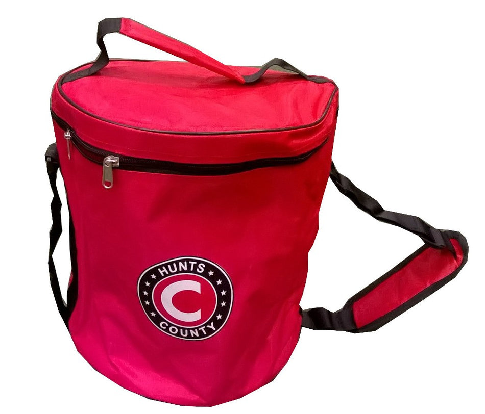 The Hunts County Ball Bag is a red cylindrical sports bag for cricket balls, featuring a zippered lid, carrying handle, shoulder strap, and a circular Hunts County logo with a large "C." It holds up to 36 balls.