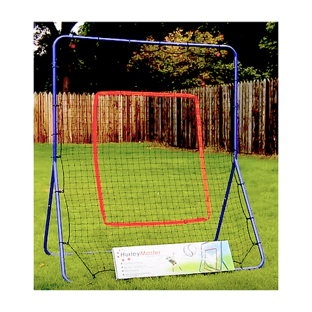 A blue and red Hurley Master Hurling Rebounder stands on a grassy lawn by a wooden fence, with a Hurley Master box at its base—ideal for hurling practice. Trees are visible in the background.