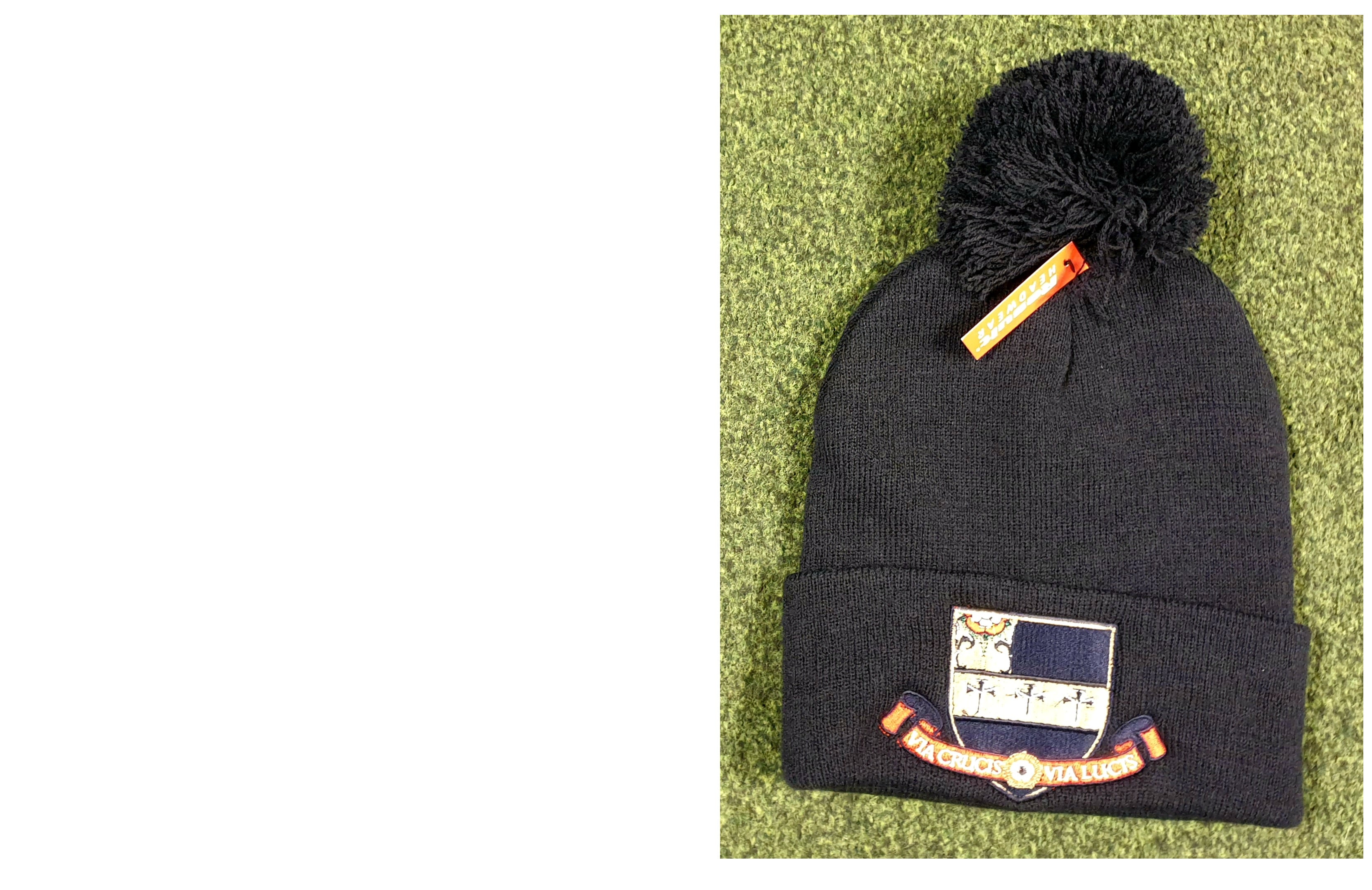 The Kings School Bobble Hat by Martin Berrill Sports, featuring a black knit design with pom-pom, embroidered logo patch, and orange tag, is displayed on a green textured surface. One size fits most.