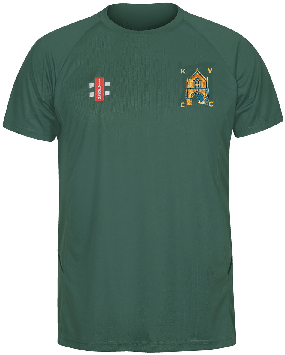 The Gray Nicolls Kingswood Village CC Matrix V2 T Shirt is a dark green, short-sleeve polyester training top with moisture-wicking fabric, a red logo on the left chest, and a detailed crest with yellow lettering and building on the right chest.