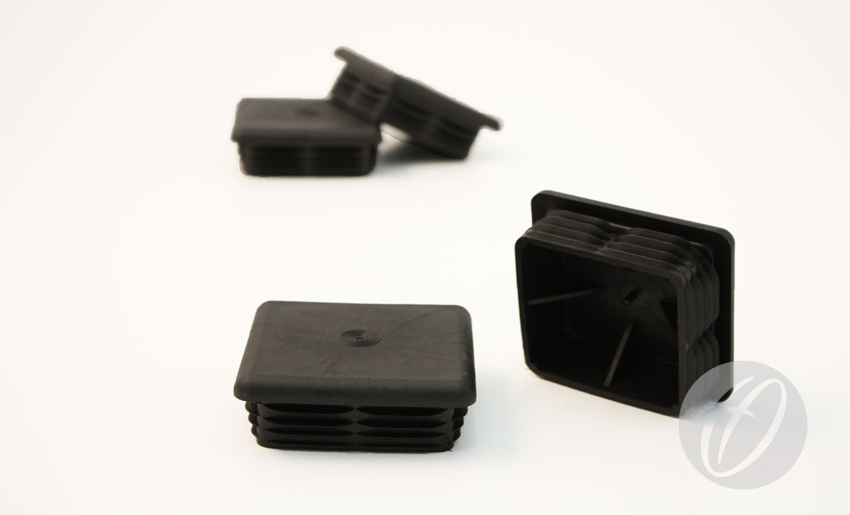 Four Harrod Sport Plastic Lids for 76mm square sockets are shown on a white surface—two stacked in the background, and two upright and sideways in front. These black, ribbed plastic lids are designed to fit 76mm square goal sockets.