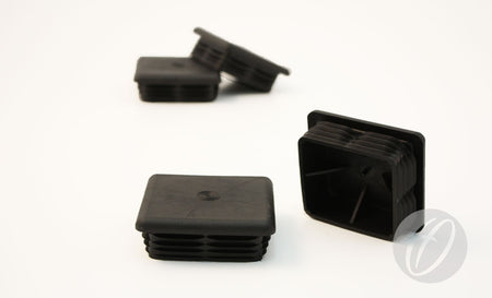 Four Harrod Sport Plastic Lids for 76mm square sockets are shown on a white surface—two stacked in the background, and two upright and sideways in front. These black, ribbed plastic lids are designed to fit 76mm square goal sockets.