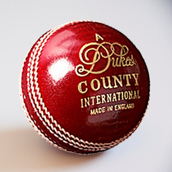 The Dukes County International A Cricket Ball (Senior) by Dukes features shiny red leather, white stitching, and gold “Dukes County International Made in England” lettering—a premium choice for serious cricketers.