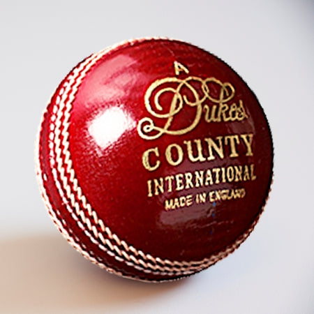 The Dukes County International A Cricket Ball (Senior) by Dukes features shiny red leather, white stitching, and gold “Dukes County International Made in England” lettering—a premium choice for serious cricketers.