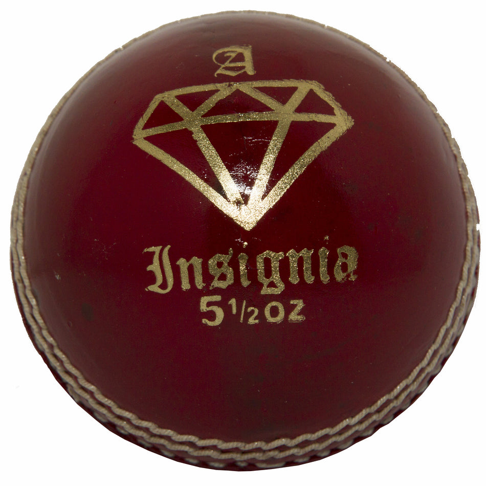 The MBS Insignia Cricket Ball by Martin Berrill Sports is a red club ball with gold markings, diamond logo, “Insignia,” and “5 1/2 oz” print. It features white hand-stitched seams for enhanced durability and performance.
