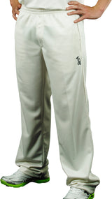 A person stands hands on hips, showing only their lower body dressed in off-white Kookaburra Pro Players Trousers Senior, a white shirt, and white athletic shoes with green soles.