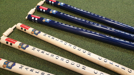 Five croquet mallets with Marlborough College on the handles—three dark blue, two white—rest on green grass. Nearby, Gray Nicolls Custom Printed Club Cricket Stumps add a personalised touch to the scene.