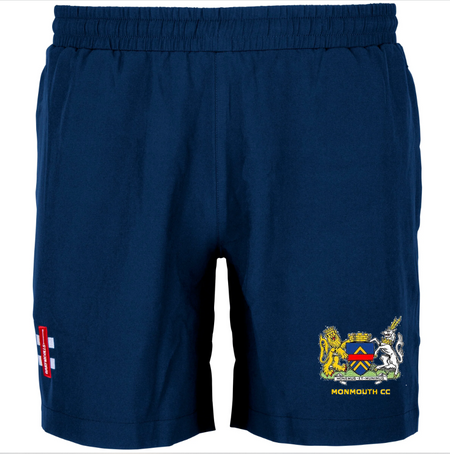 The Gray Nicolls Monmouth CC Junior Dark Navy Training Shorts feature an elastic waistband, a colorful crest with lions and "MONMOUTH CC" on the right leg, and a red-and-white England cricket logo on the left—ideal for practice.