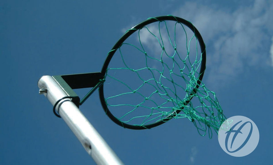 A low angle view of a Harrod Sport Regulation Netball Post - Freestanding, 16MM Ring, with a green net against a clear blue sky and a watermark in the lower right corner.