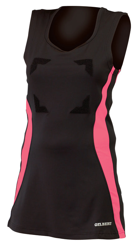 Women's netball uniform featuring the Gilbert Eclipse Netball Dress by Gilbert in Black/Pink, with pink side panels, V-neck, GILBERT logo near the hem, and chest patches for netball position bibs.