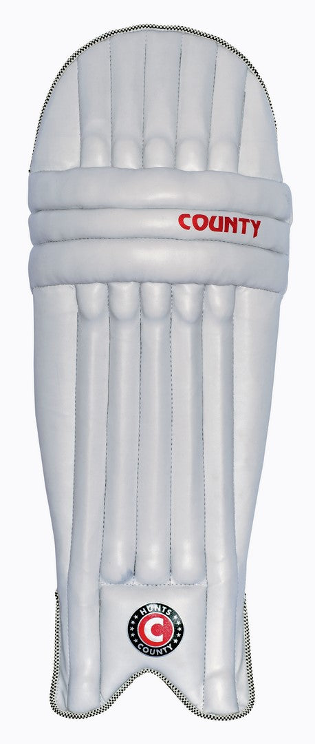 The Hunts County Neo Junior Batting Pads are white with vertical padding, featuring the Hunts County name in red and a round black, red, and white logo near the bottom—ideal for young cricketers.
