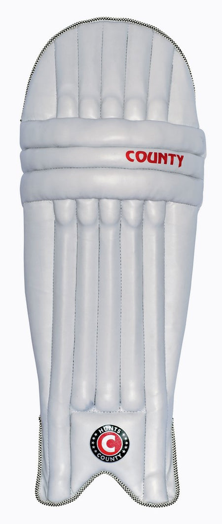 The Hunts County Neo Junior Batting Pads are white with vertical padding, featuring the Hunts County name in red and a round black, red, and white logo near the bottom—ideal for young cricketers.