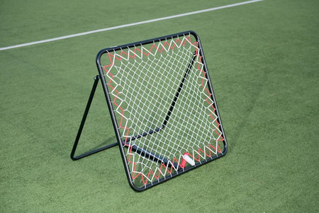 The Precision Training Precision Pro Rebounder, featuring an adjustable angle and sturdy black metal frame with red ties, is set up on a green field with white markings—ideal for football training sessions.