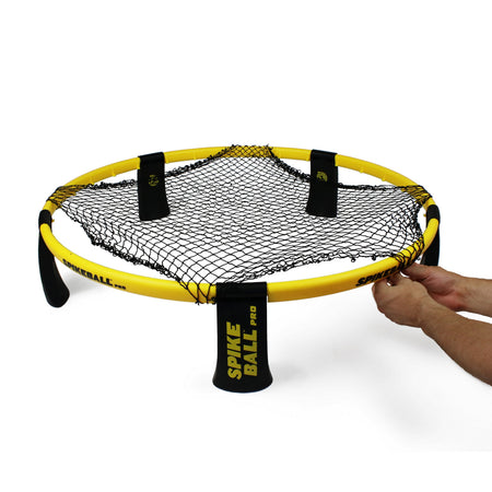 A person's hands assemble a round yellow Kankakee Spikeball Pro Set with black legs and a taut net in the center, set against a white background.