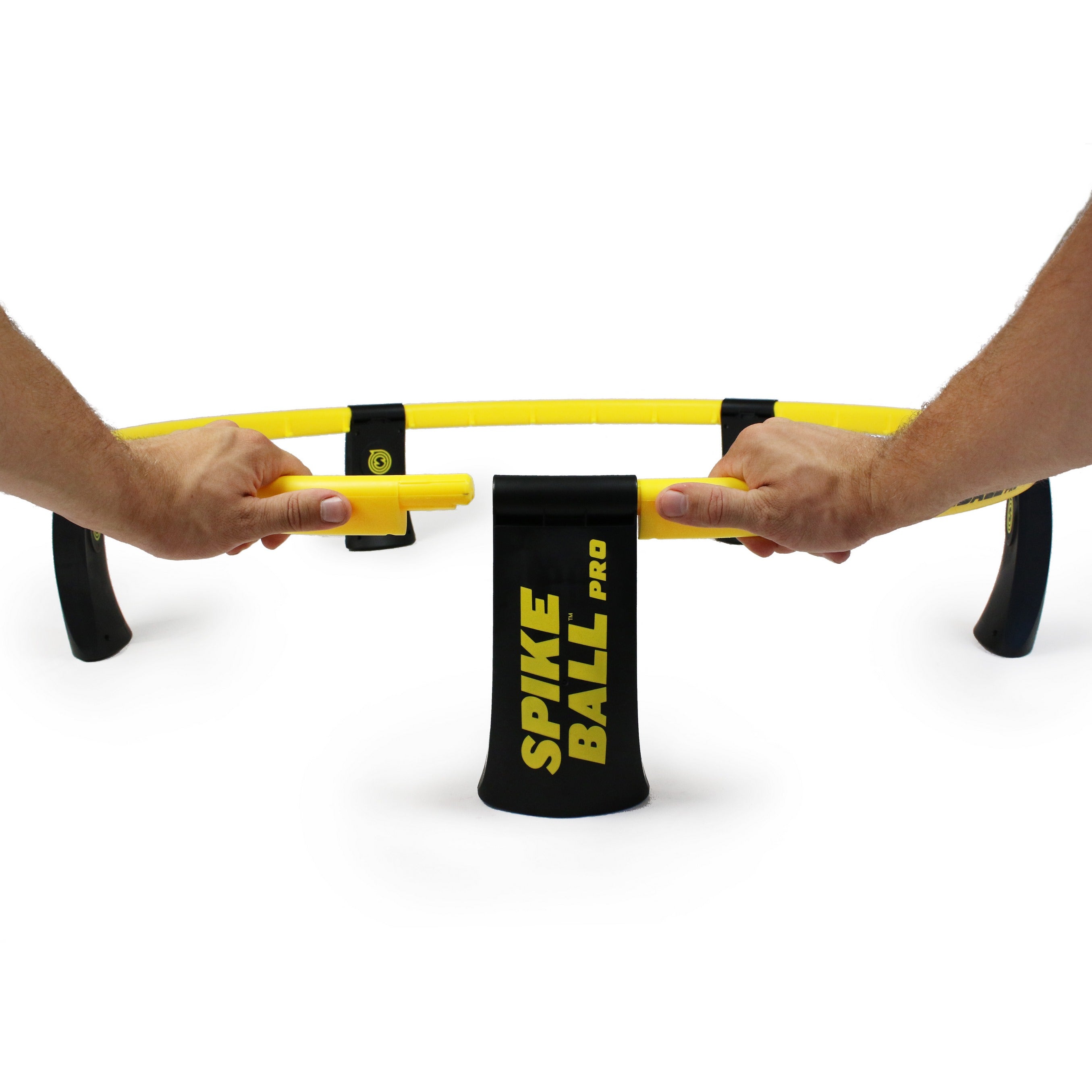 Two hands assemble a yellow and black Kankakee Spikeball Pro Set, connecting the frame pieces. A Kankakee Spikeball Pro branded drawstring bag sits in the center—everything needed comes in this official set.