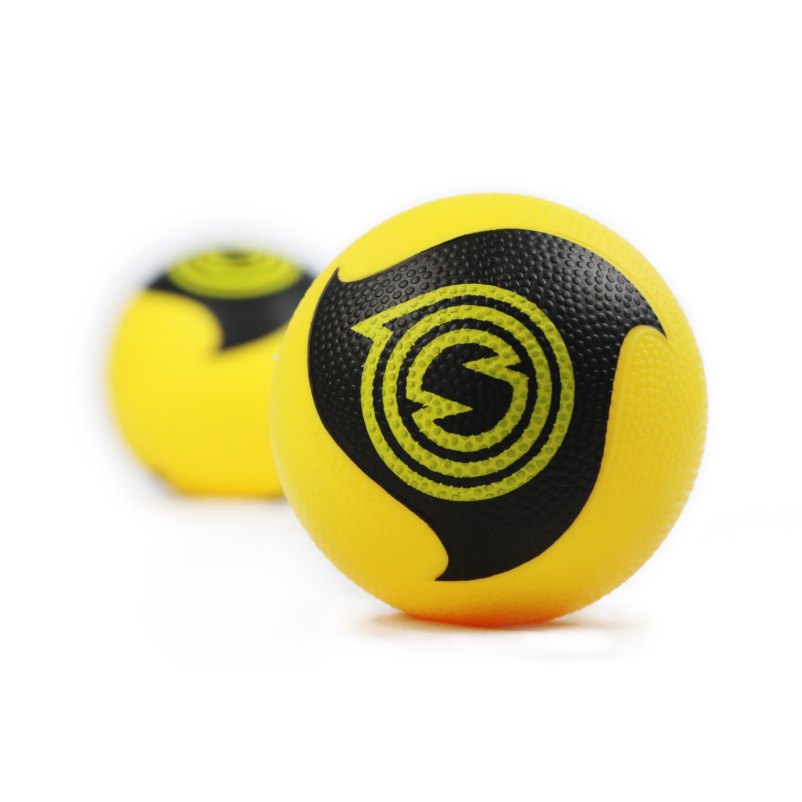 A close-up shows a yellow ball with a black and yellow spiral design and textured surface from the Kankakee Spikeball Pro Set; another similar ball from the set is blurred in the background on a white surface.
