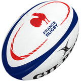 The Gilbert France Replica Rugby Ball features white panels with blue details, red curved lines, and a bold red rooster logo. "FRANCE RUGBY" appears beside the rooster and "GILBERT" is partially visible—perfect for fans of French rugby.